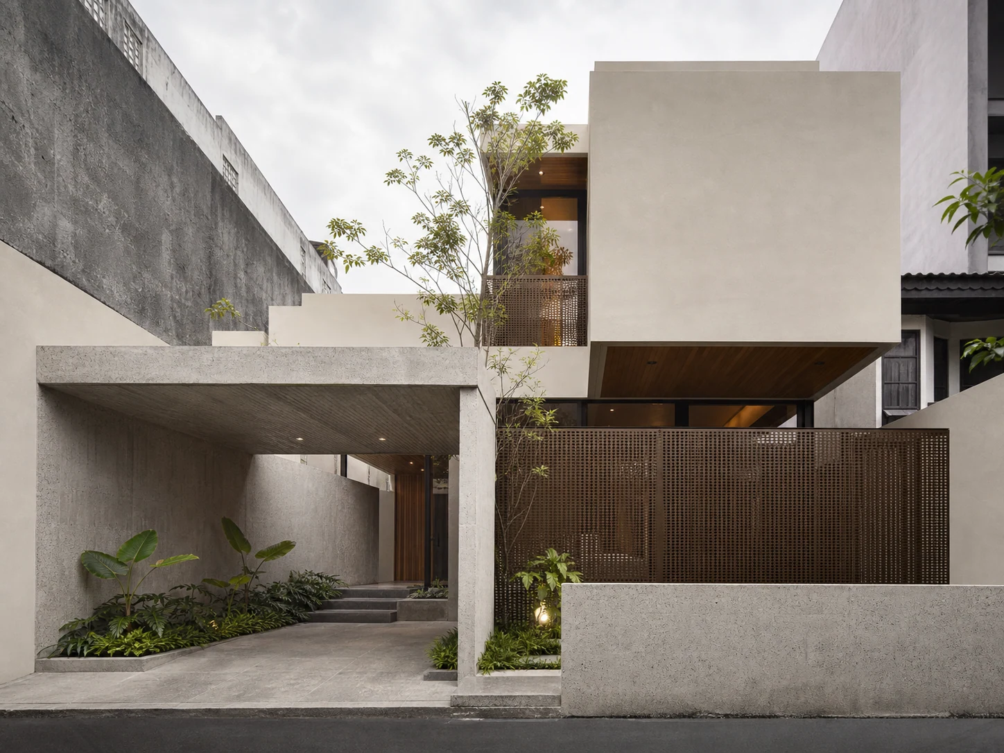 Hunian urban modern dengan massa plaster terang, portal beton, dan kisi metal perunggu